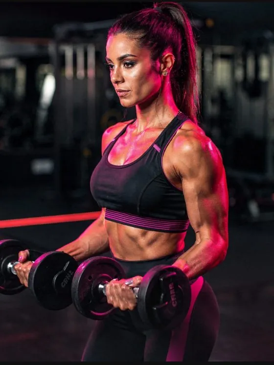 Mulher treinando com halteres na academia, iluminação magenta